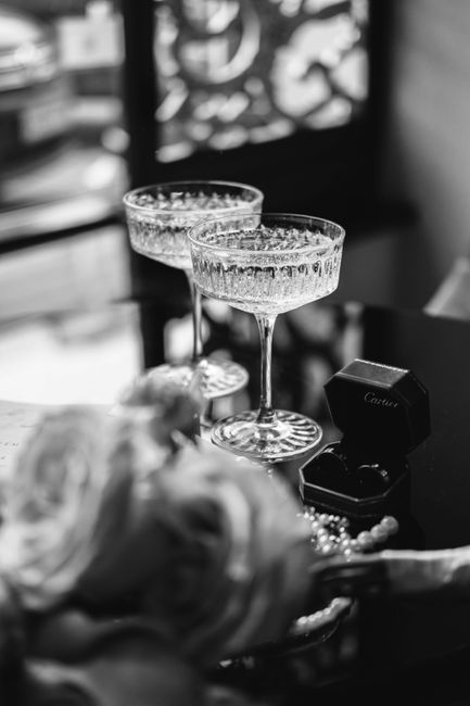 Black and white photo of champagne glasses and a Cartier jewelry box, epitomizing class and elegance.