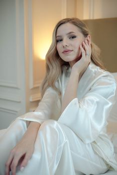 A poised woman in satin lounge attire seated indoors, exuding elegance.
