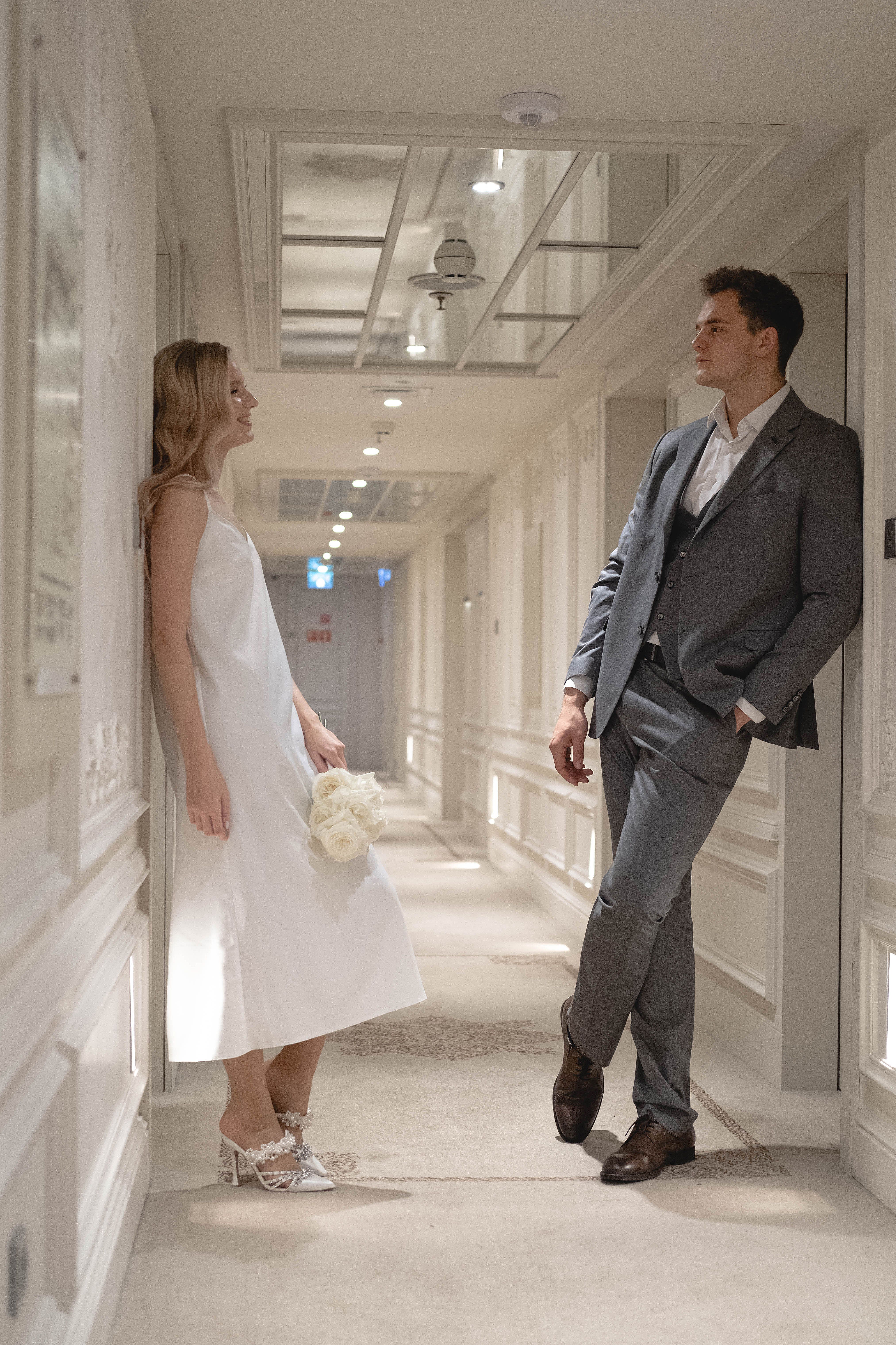 A romantic couple in a hallway, bride in white dress and groom in gray suit.