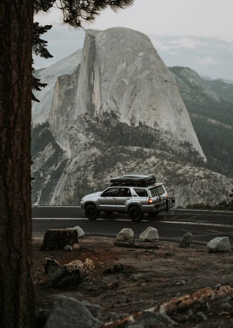 Silver SUV drives by Yosemite's iconic Half Dome, showcasing adventure and travel.