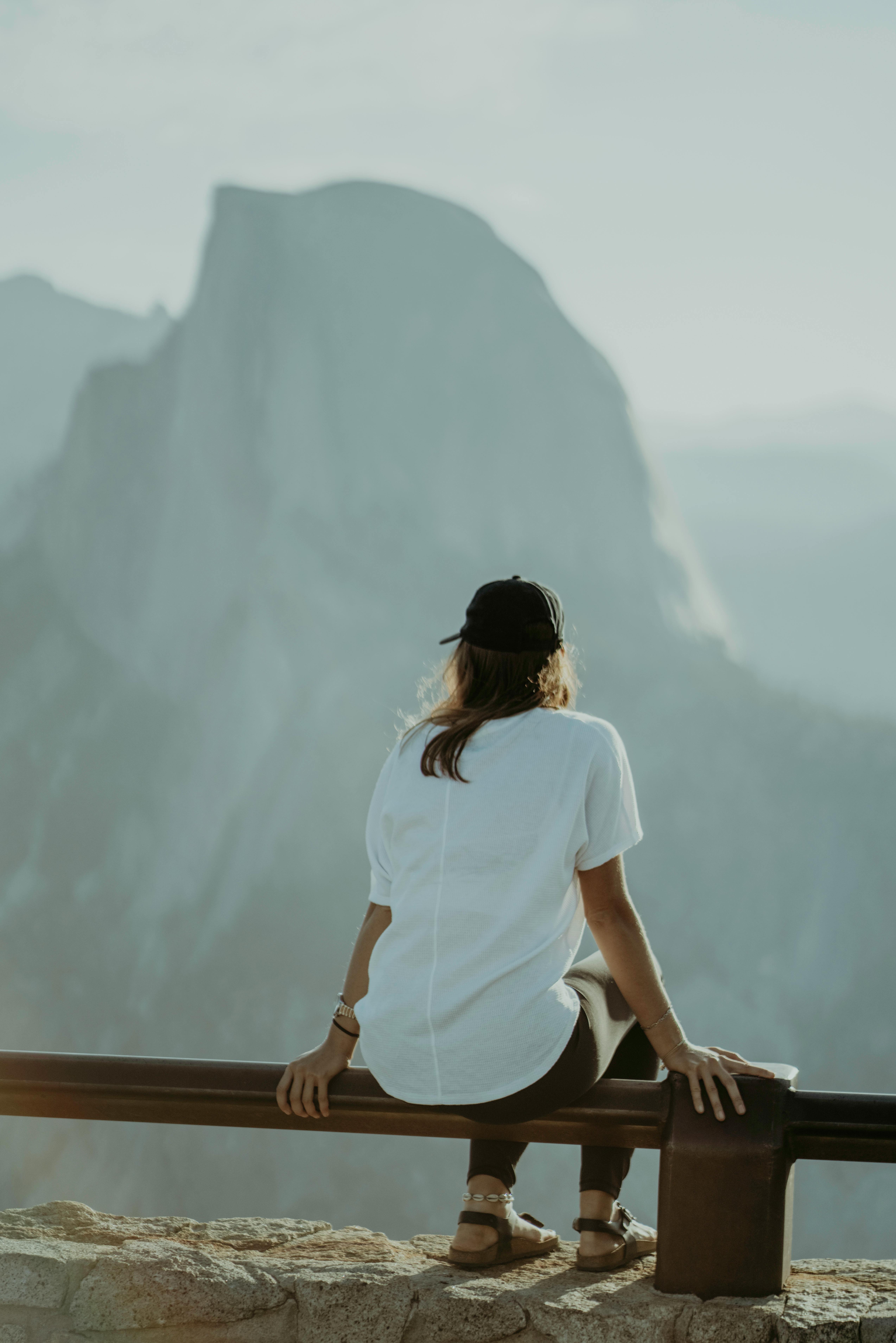 A woman sits on a railing, enjoying a serene mountain view at sunset in Yosemite National Park.
