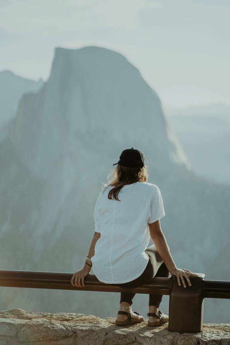 A Shot From Behind Of A Female Sitting And Looking At Mountain Peak 