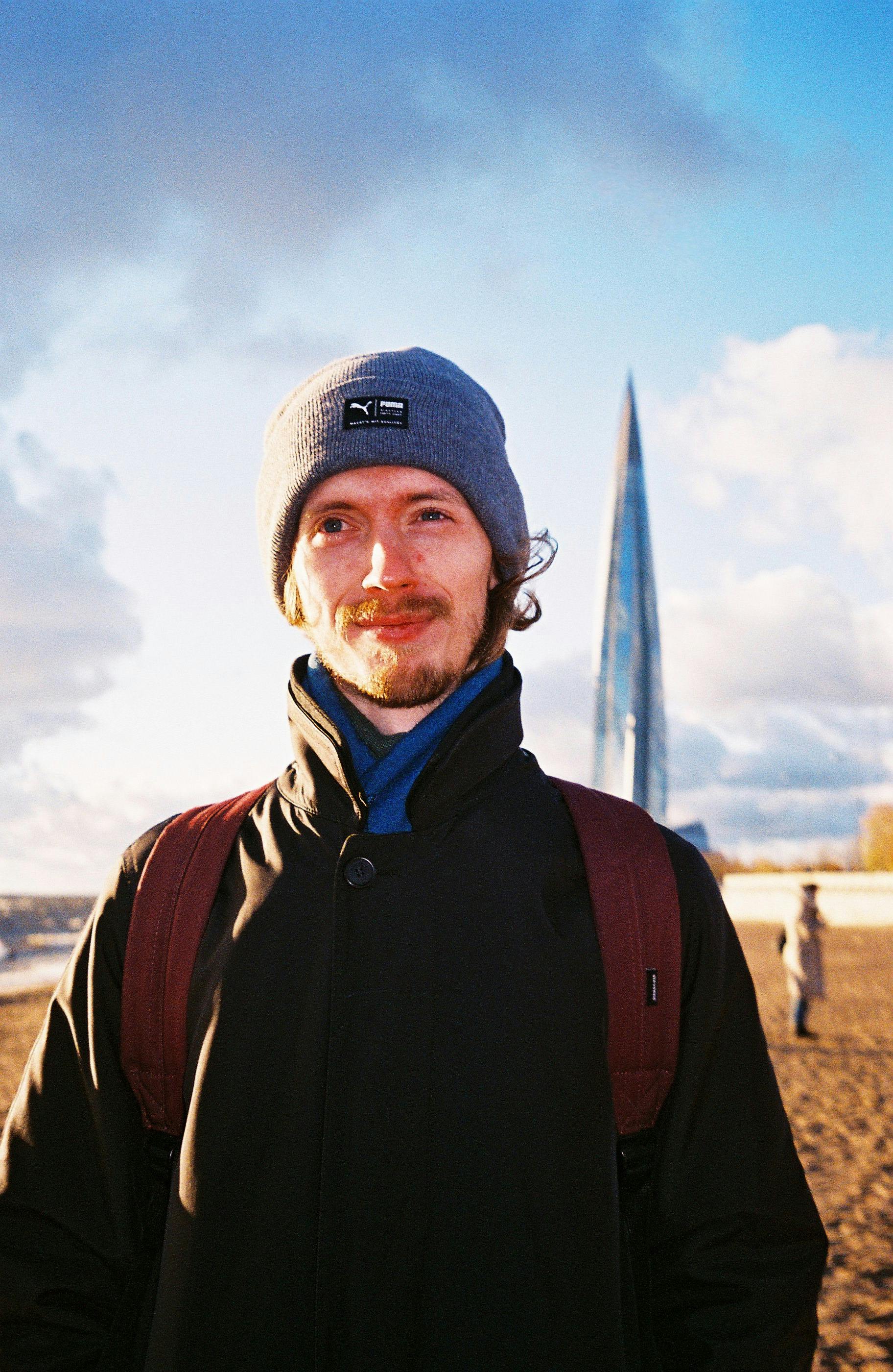 Portrait of a smiling man in a beanie by Lakhta Center, St. Petersburg.