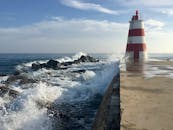 在明亮的天空下，海浪拍打着岩石海岸，岸边矗立着一座条纹灯塔