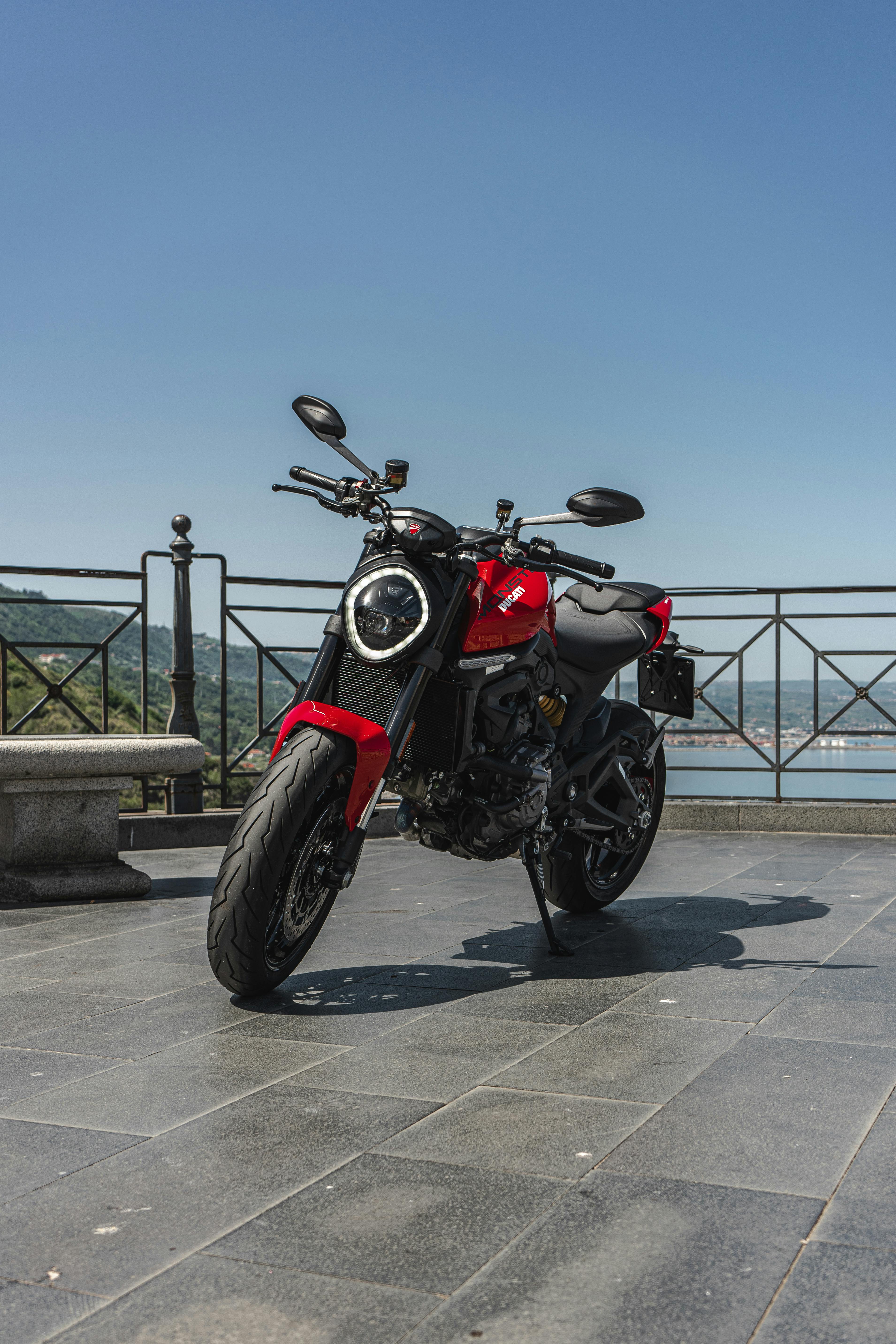 Free A red motorcycle parked on a scenic terrace with coastal views on a clear day. Stock Photo