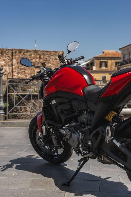 Free A bright red motorcycle is parked in a sunlit urban area under clear blue skies. Stock Photo