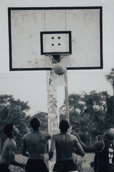 Monochrome photo of men playing basketball outdoors, focusing on hoop action.