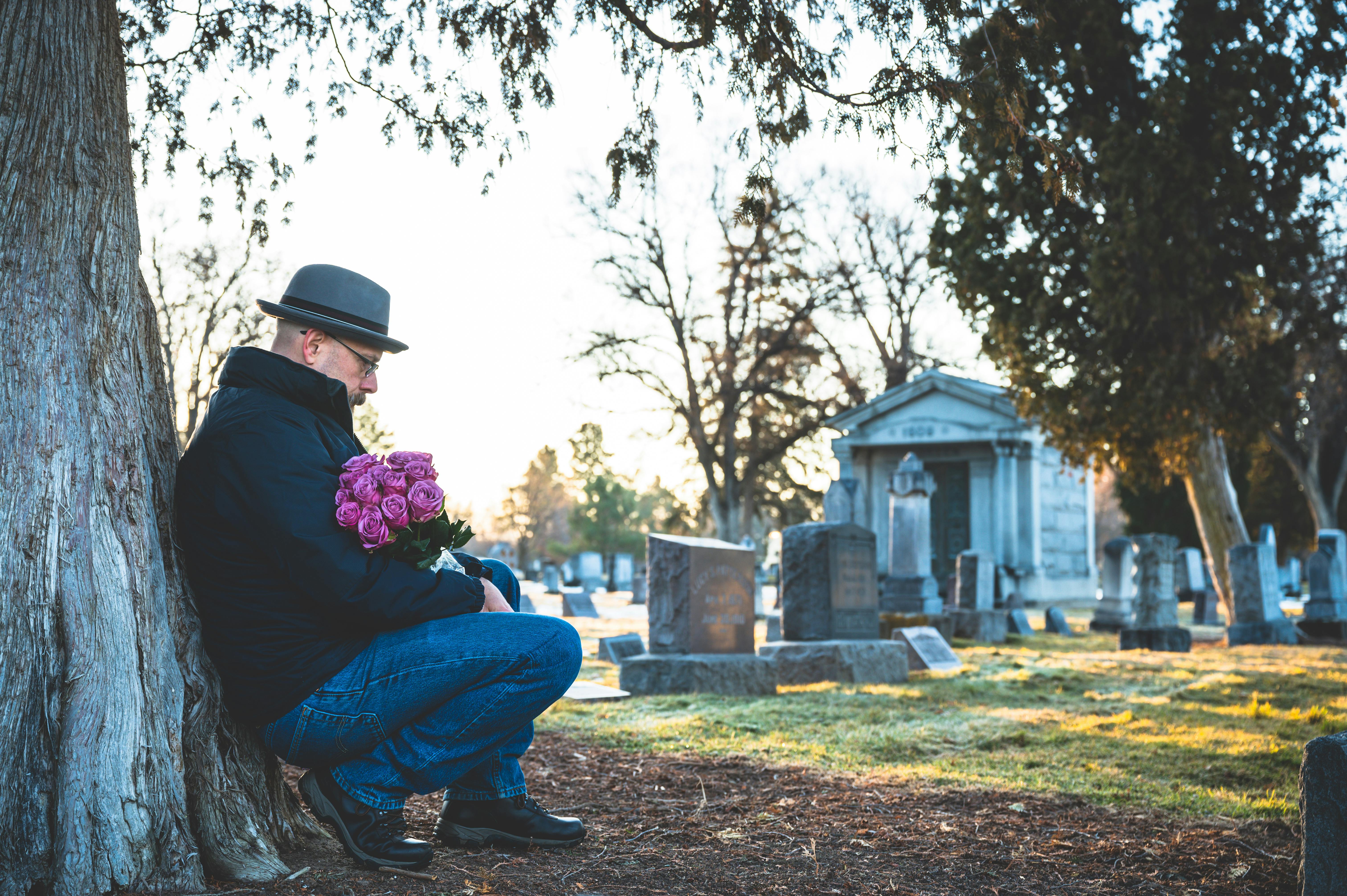 Free Man in Jacket Leaning on a Tree While Holding Flowers Stock Photo