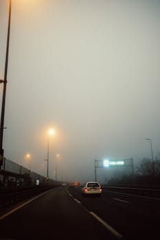 A foggy night on the highway with automobiles and bright streetlights illuminating the road.