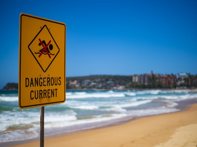 Sandy Beach With Waves And Yellow Sign With Warning