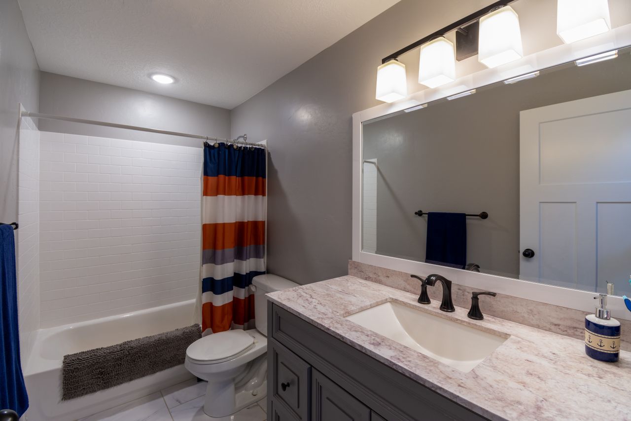 Clean modern bathroom with bathtub, toilet, vanity sink, and large mirror