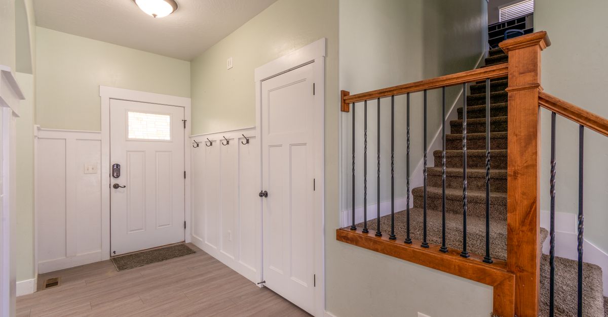 Bright entryway featuring wooden stairs, white door, and wall-mounted coat hooks.