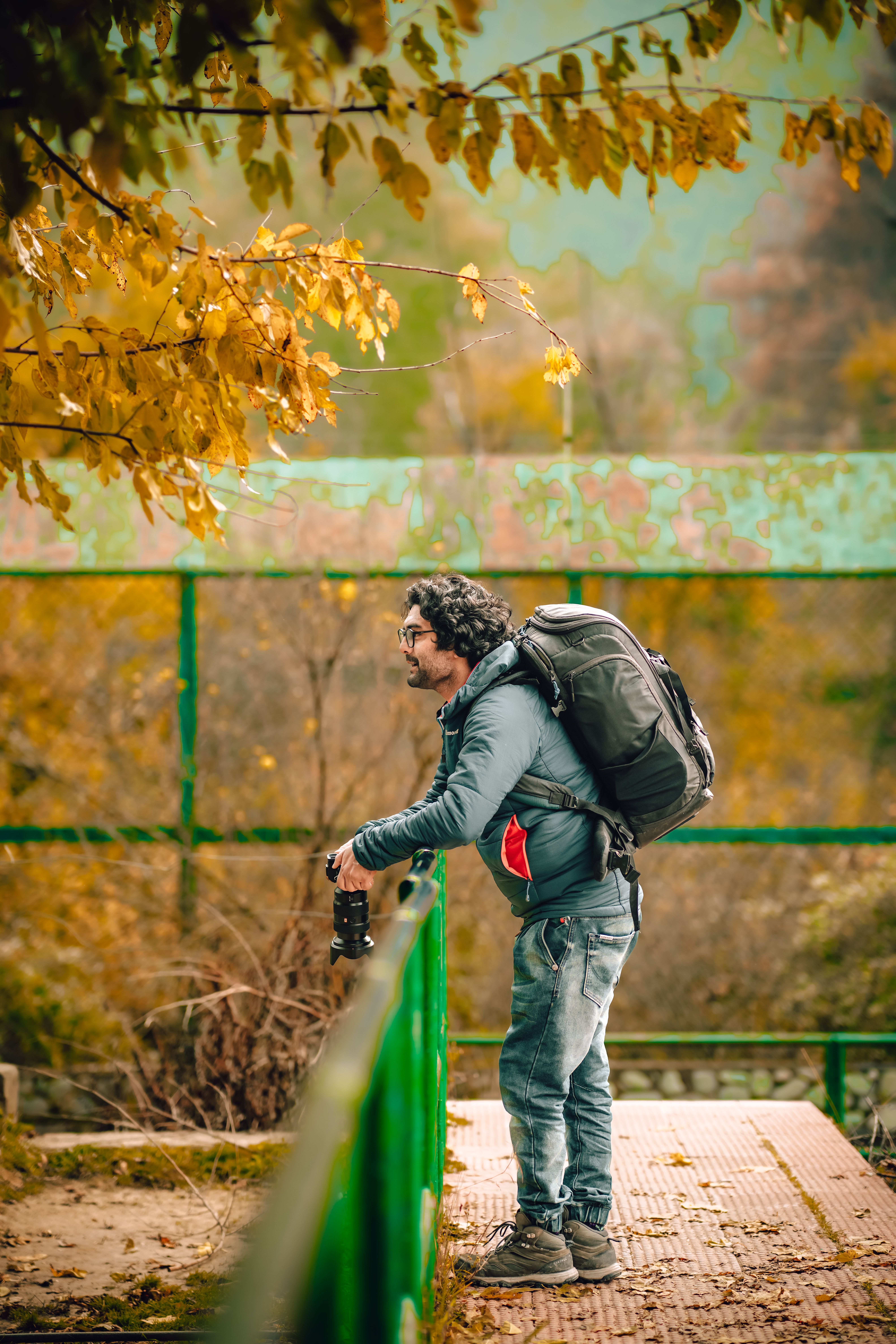 Man with camera and backpack gazes at fall foliage in a serene park setting.