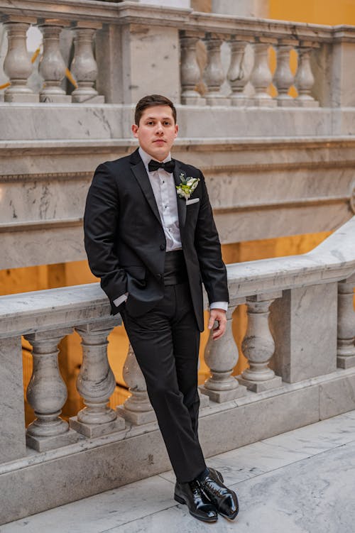Man in Black Tuxedo Leaning on a Concrete Railings while Seriously Looking at the Camera