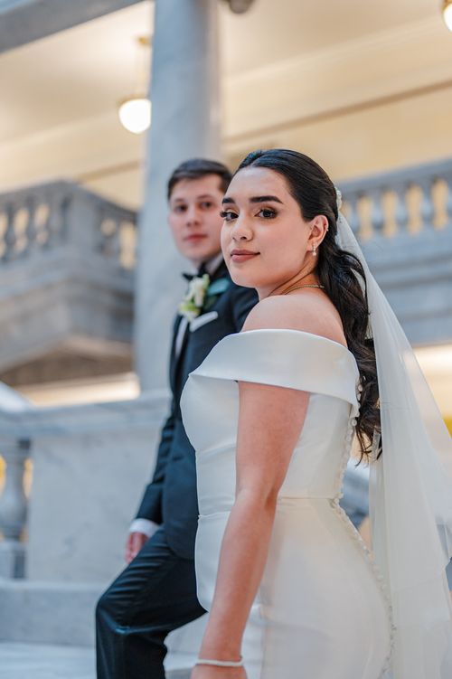 Free A bride and groom pose elegantly on a staircase in a luxurious venue, capturing their special day. Stock Photo