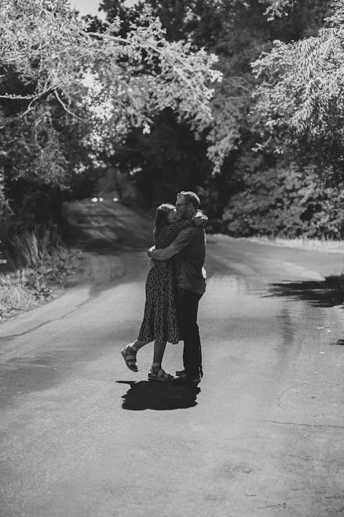 Man and Woman Kissing on Road in Grayscale Photography