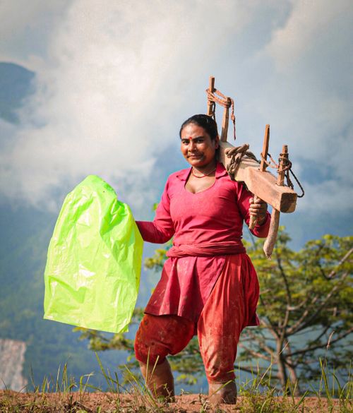 Free Nepali woman farmer in traditional clothing holding equipment on a bright day in rural landscape. Stock Photo