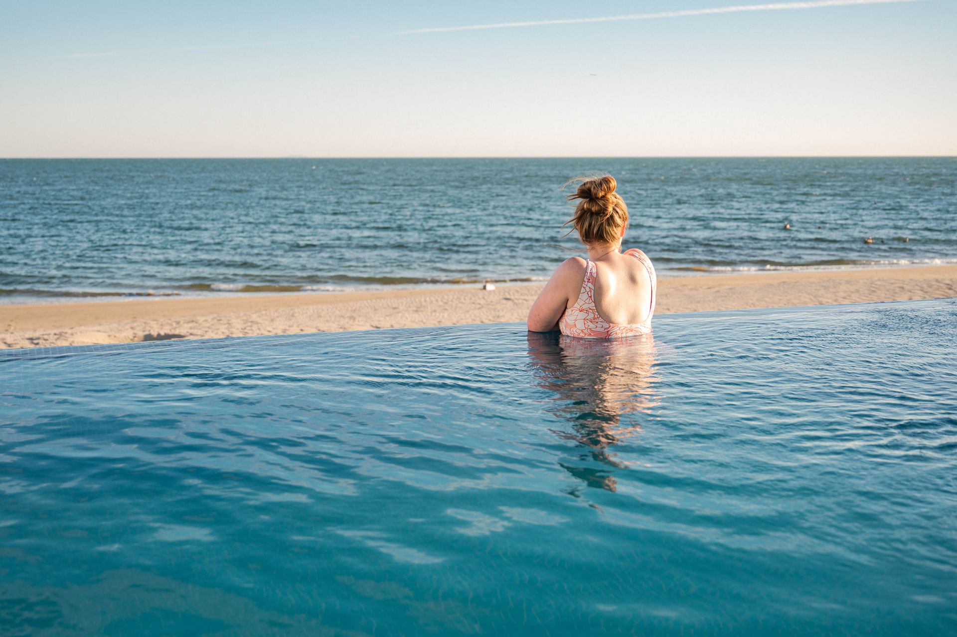 Woman unwinds in infinity pool with serene ocean view, capturing tranquility.