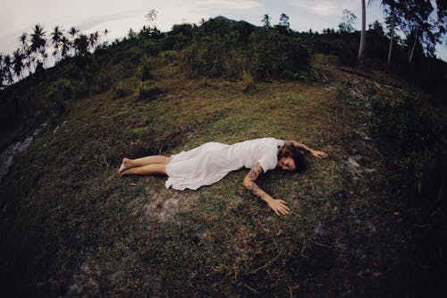 Woman in White Dress Lying on Green Grass Field