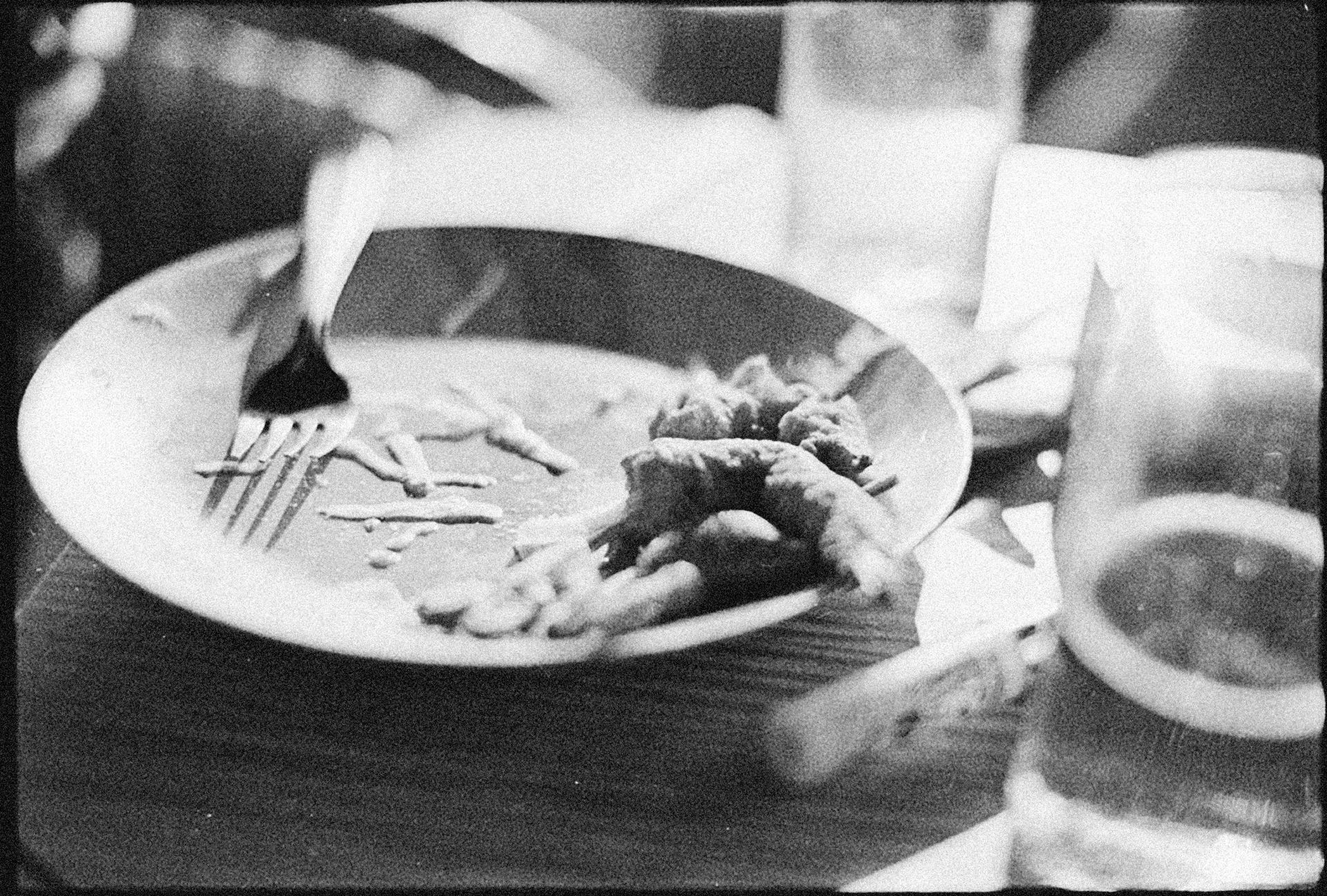 Black and white image of a plate with leftover food and a fork, creating a moody setting.