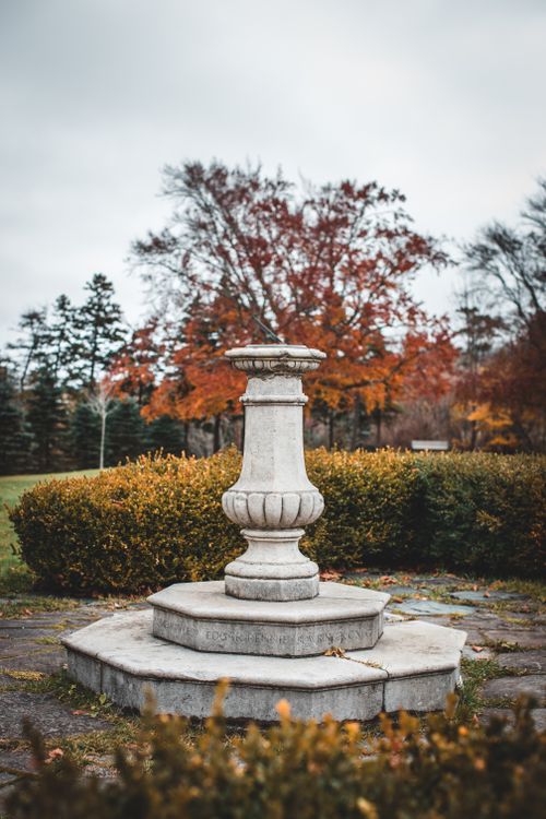 Free A classic stone column surrounded by colorful autumn foliage in a serene park setting. Stock Photo