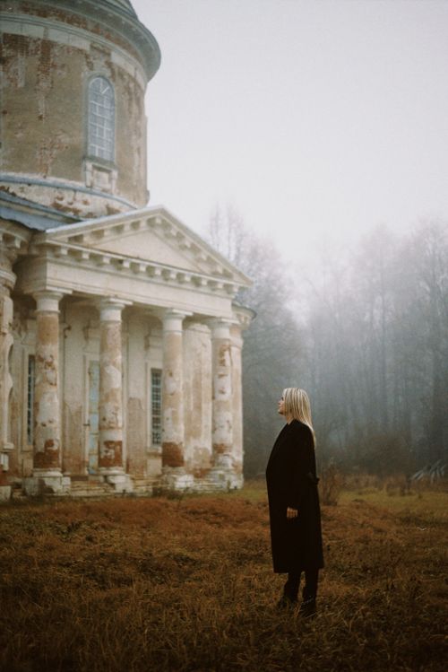 Free A woman in a black coat stands near an abandoned historic building in autumn fog. Stock Photo