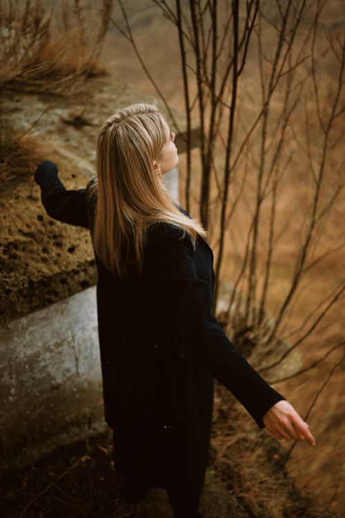 Free Woman with arms outstretched outside in autumn, wearing a black coat. Stock Photo