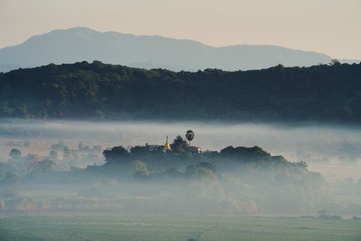 Aerial view of misty hills and temple surrounded by a serene landscape at dawn.