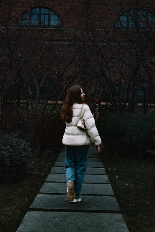 Back View of a Woman in a Puffer Jacket Walking on a Pathway