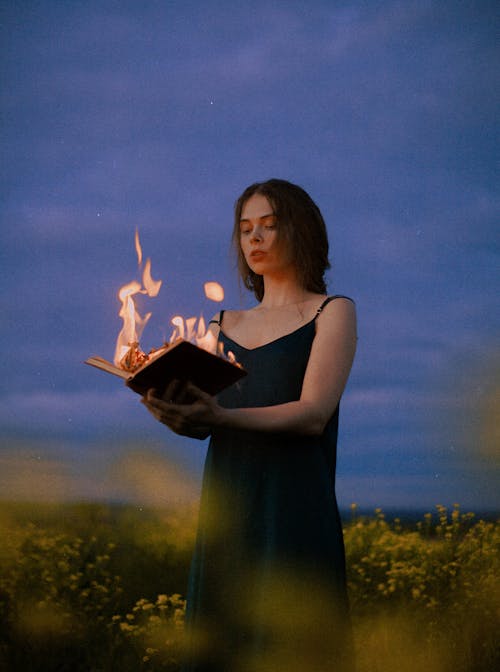 Woman Holding Burning Book on a Field 