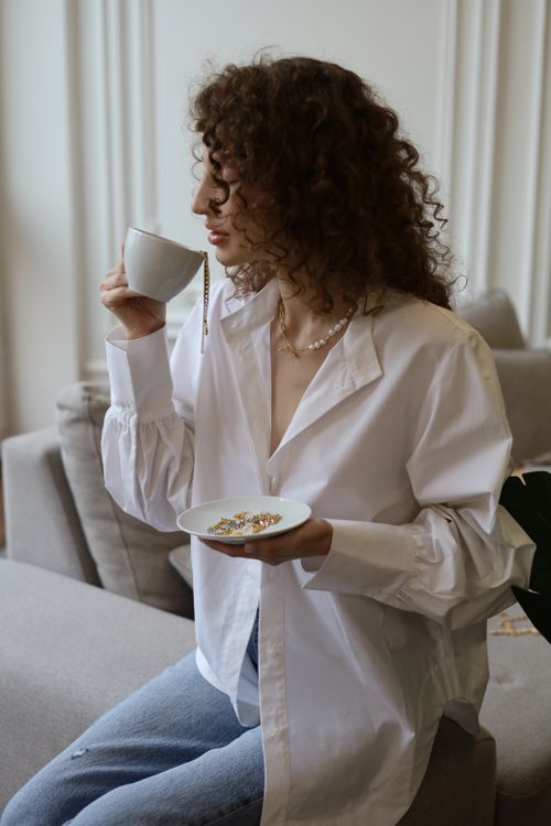 Free Woman sitting on couch, sipping from a cup while holding a jewelry plate. Stock Photo