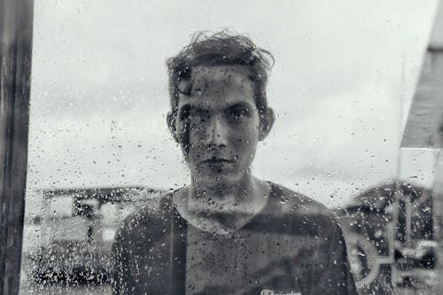 Man Standing Behind the Window with Drops on It