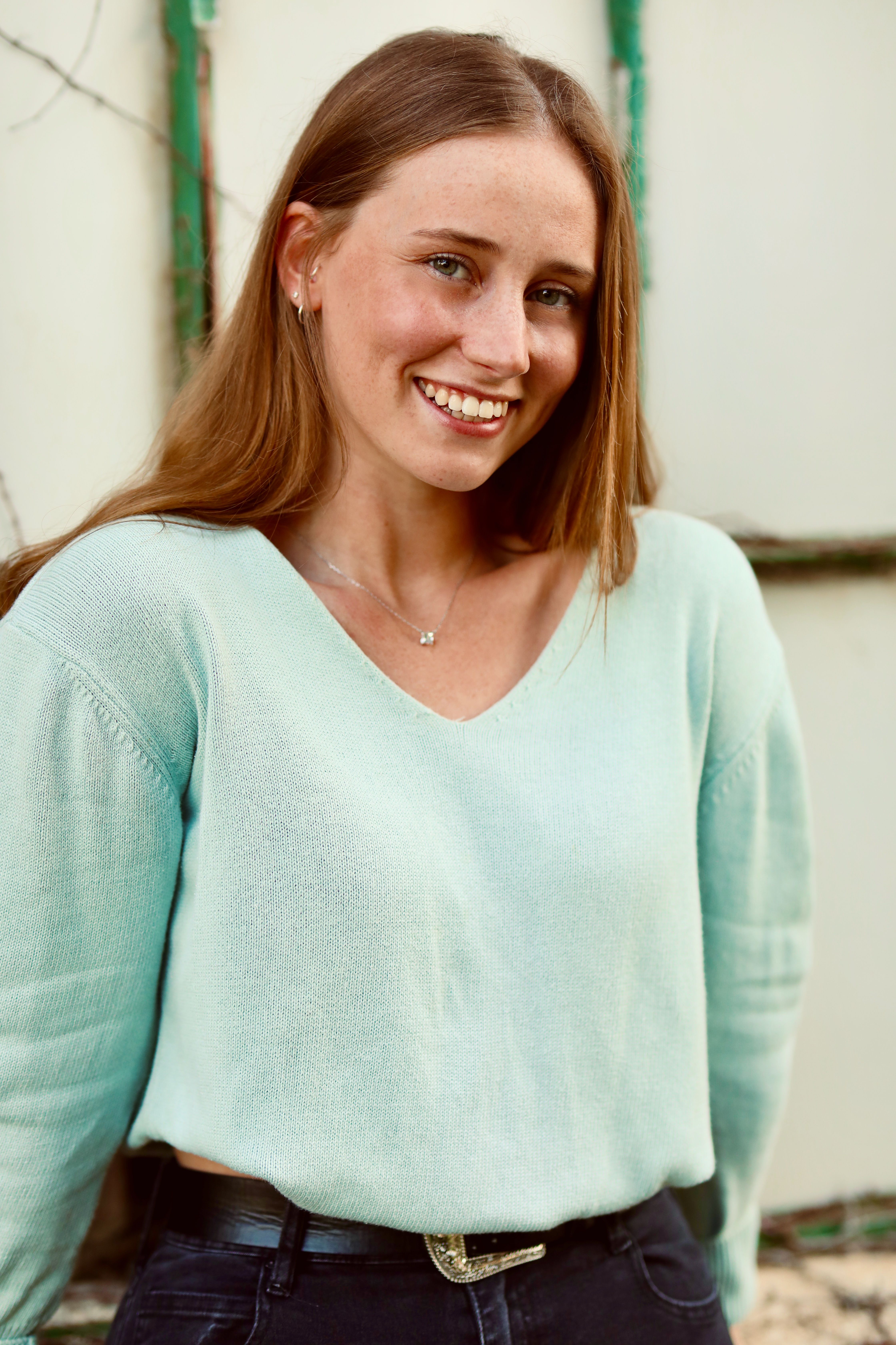Portrait of a smiling woman outdoors wearing a blue sweater on a sunny day.