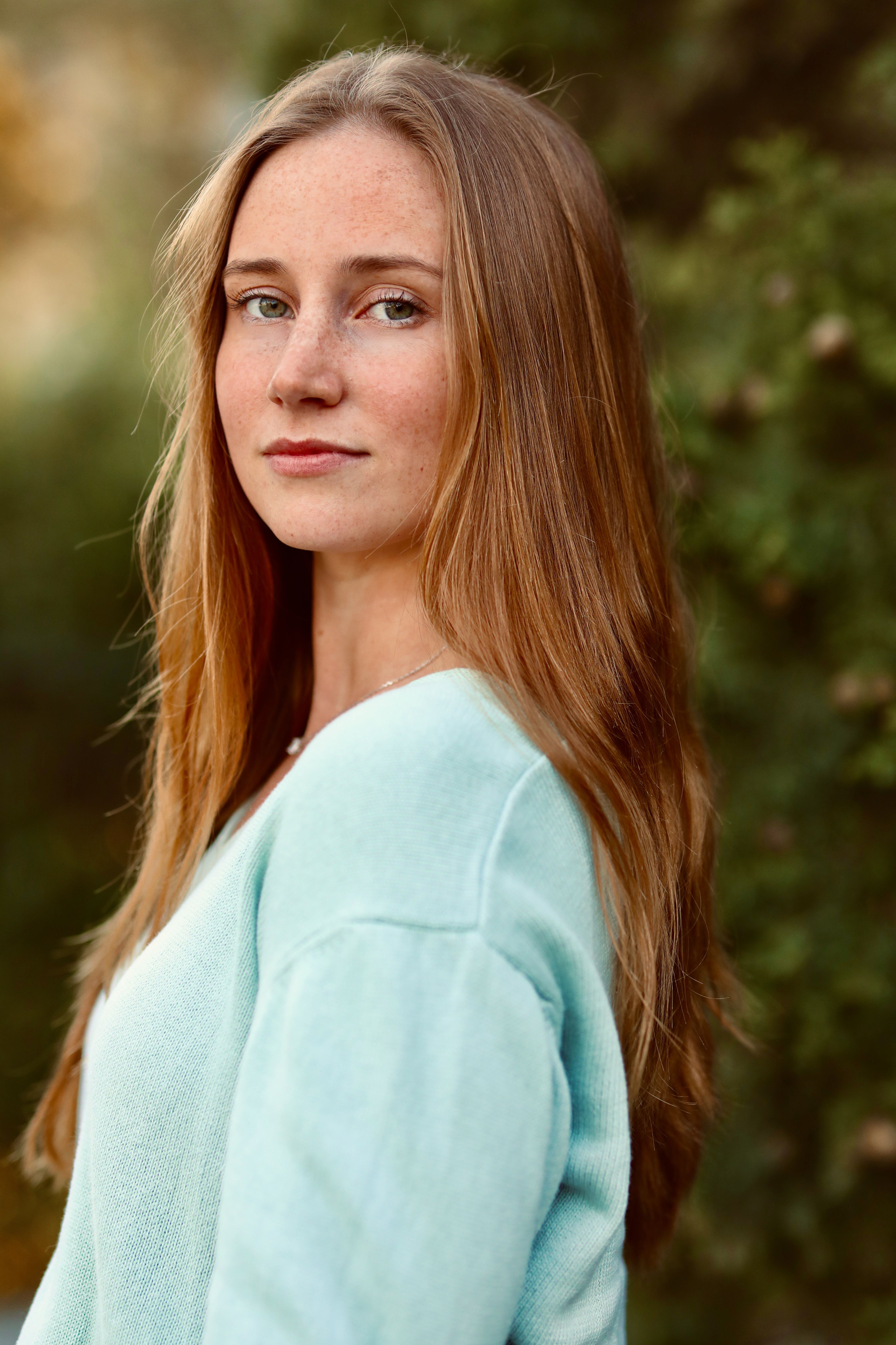 Serene portrait of a young woman with long hair in a blue shirt, set against a natural blurred background.