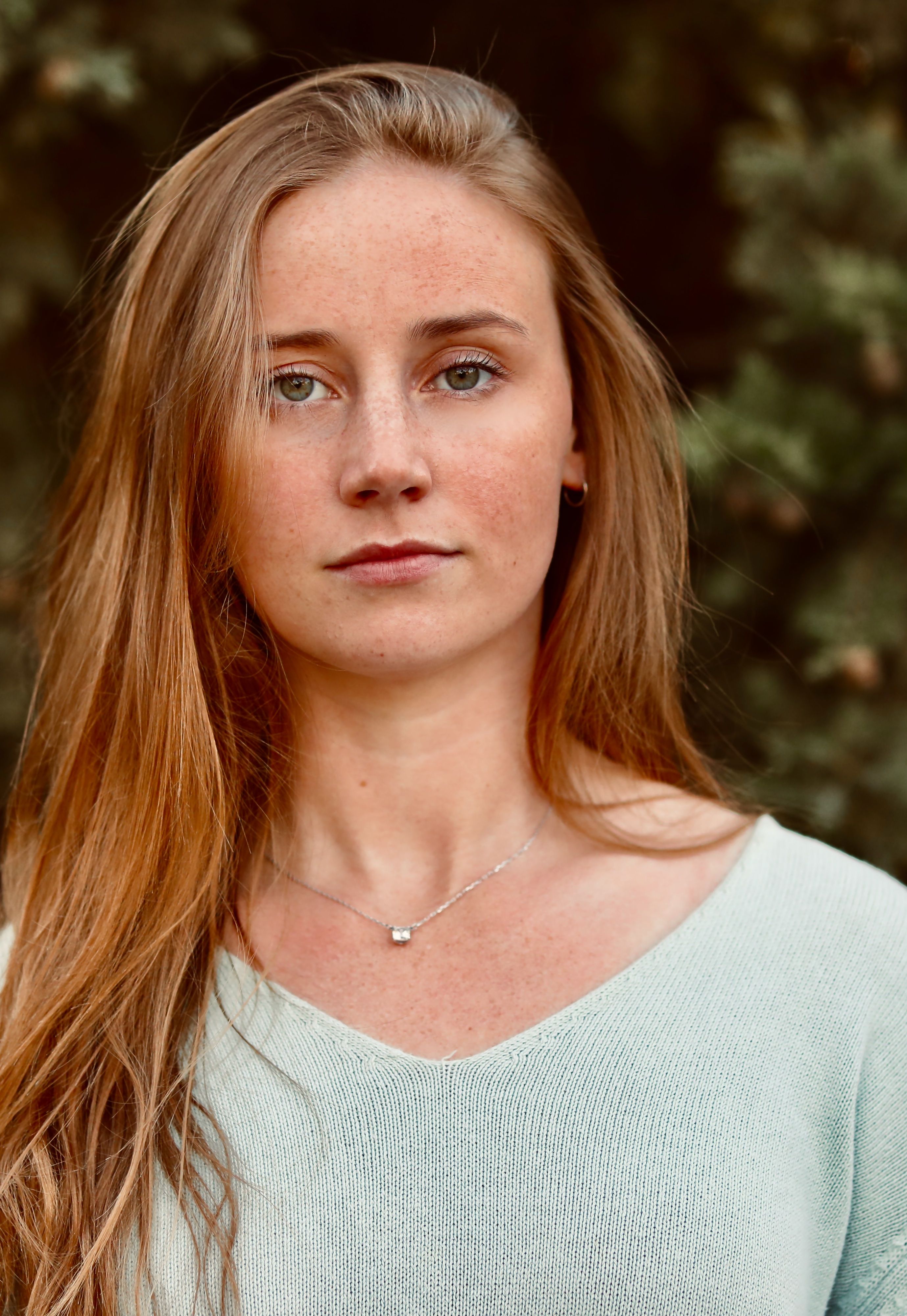 Close-up portrait of a young woman with long hair and necklace outdoors in natural light.