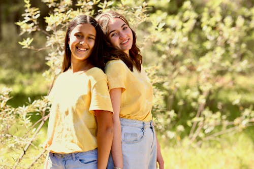 Women in Yellow Shirt Standing Back to Back while Smiling at the Camera