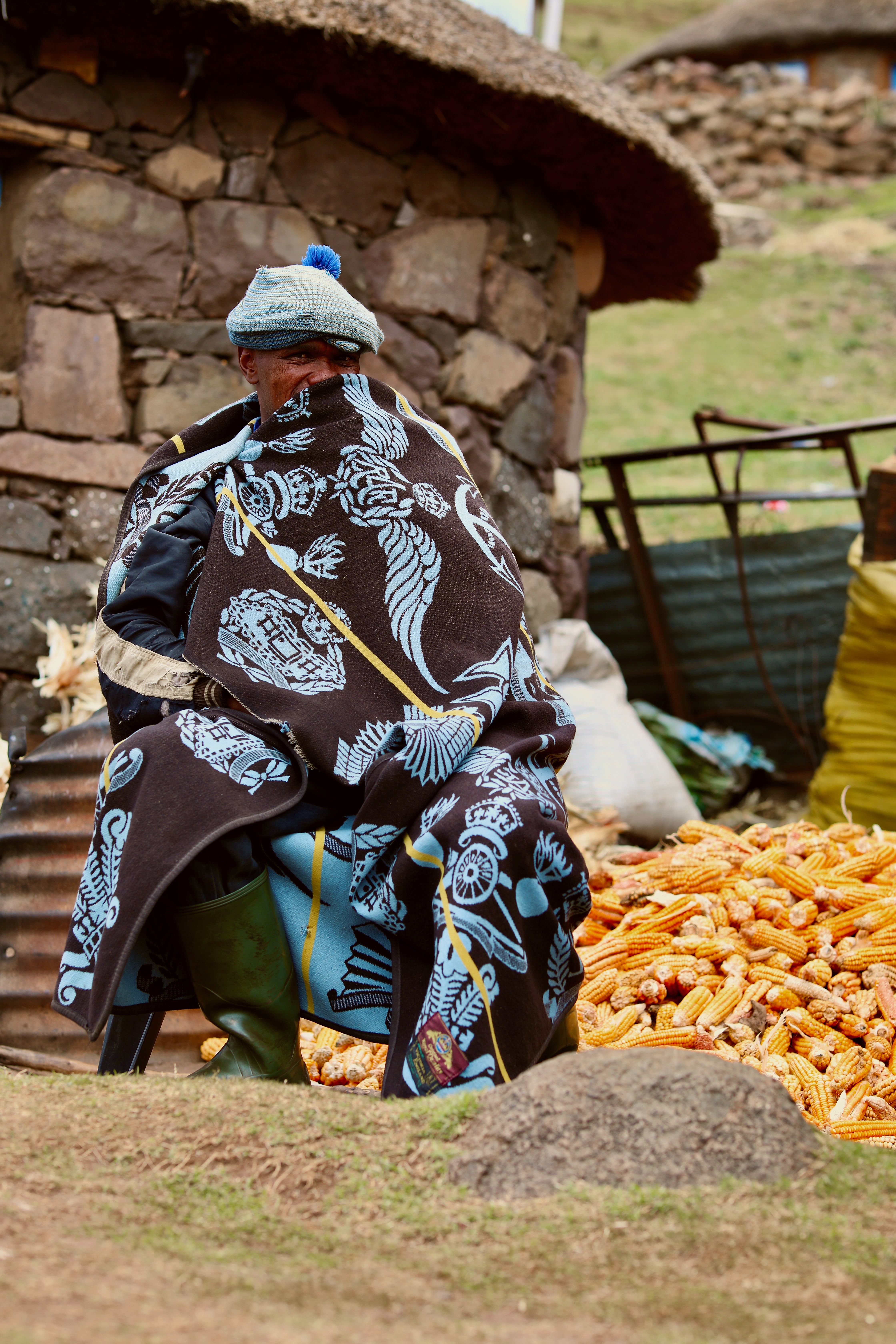 Man in traditional coat sitting by pile of corn, Lesotho
