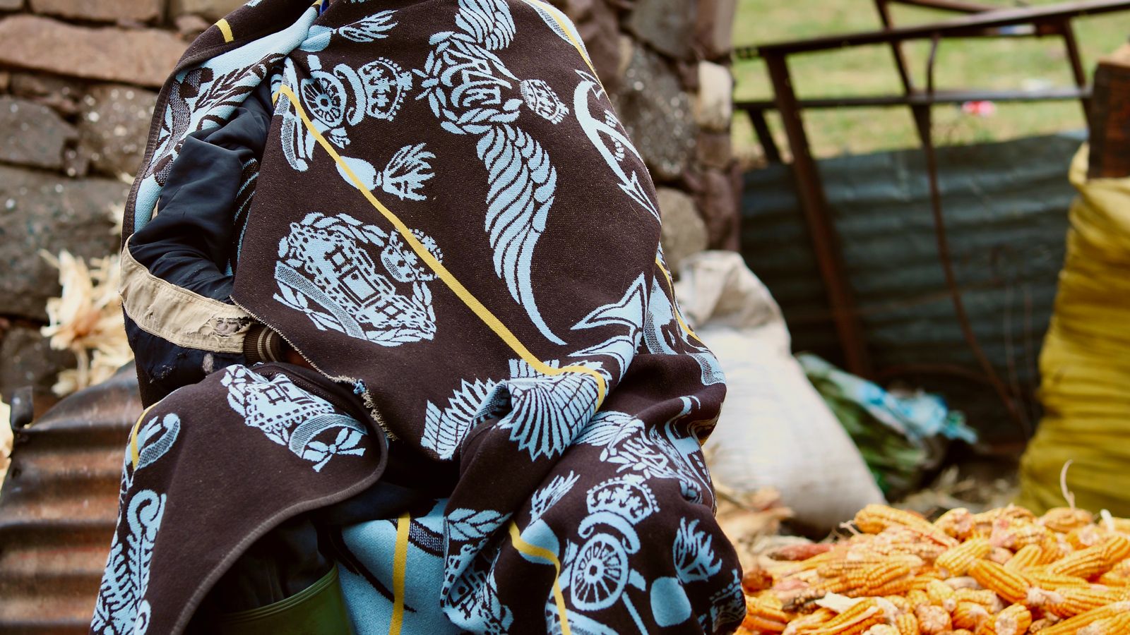 Man in traditional coat sitting by pile of corn, Lesotho