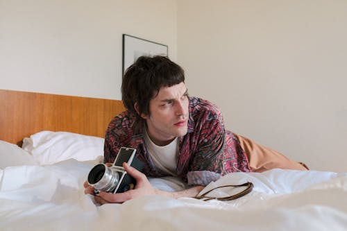 Free Man Laying in Bed on Stomach and Holding Analog Camera Stock Photo