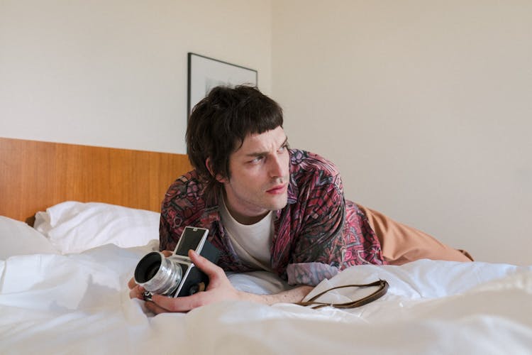 Man Laying In Bed On Stomach And Holding Analog Camera