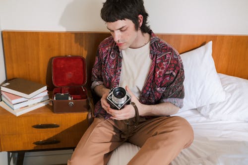 Teenage Boy Sitting in Undone Bed and Setting Vintage Camera