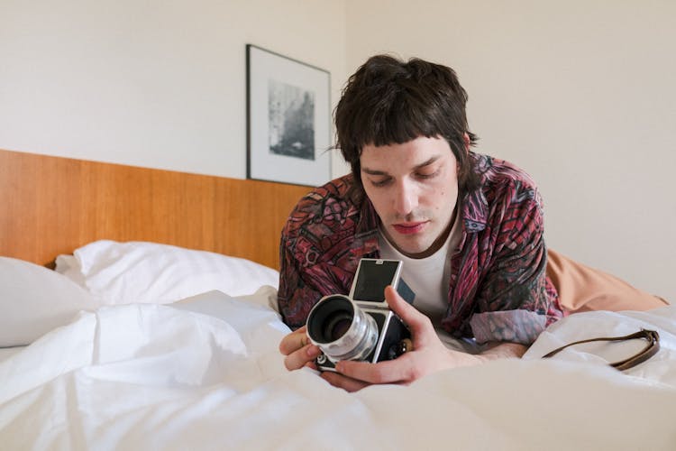 Man Laying On Bed And Looking At Analog Camera