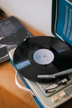A vintage turntable playing a vinyl record next to a stack of albums.