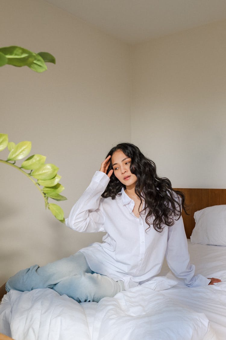 Beauty With Long Curly Hair Sitting In Bed With Hand In Hair