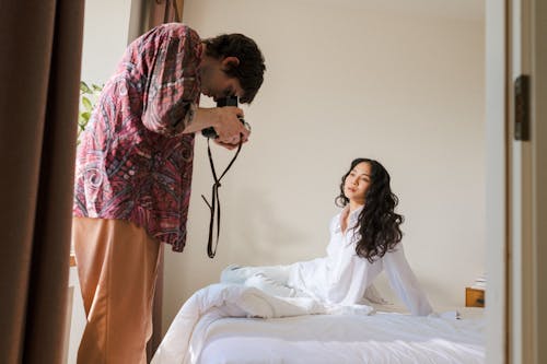 Man Taking Picture of a Woman Sitting on Bed