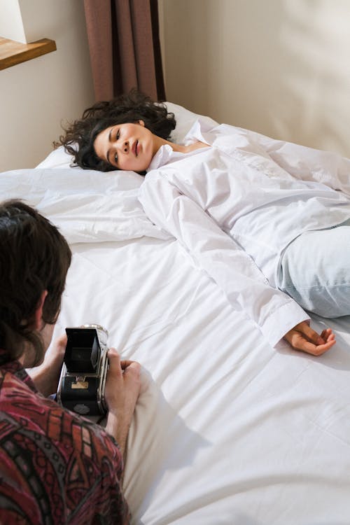 Man Taking Picture of a Woman Laying on a Bed