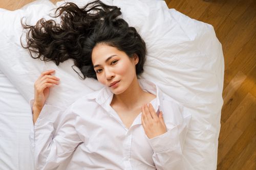 Free A serene portrait of a woman lying on a bed, looking at the camera with soft natural lighting. Stock Photo