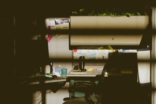 在柔和的灯光下，光线昏暗的办公隔间里配有电脑、椅子、桌子和室内植物