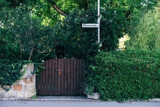 Rustic wooden gate surrounded by lush greenery and street sign on a summer day.