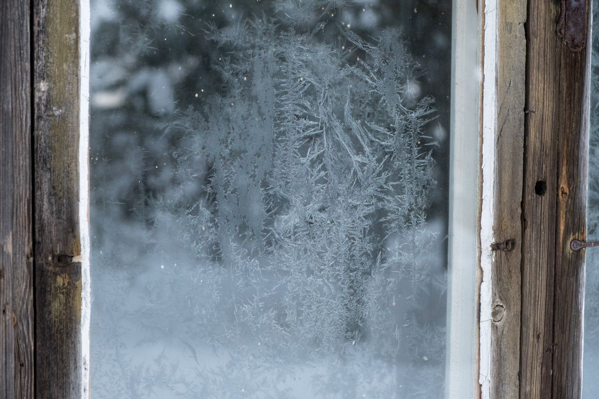 Fenster mit rustikalem Holzrahmen und winterlichen Frostmustern auf der Glasscheibe
